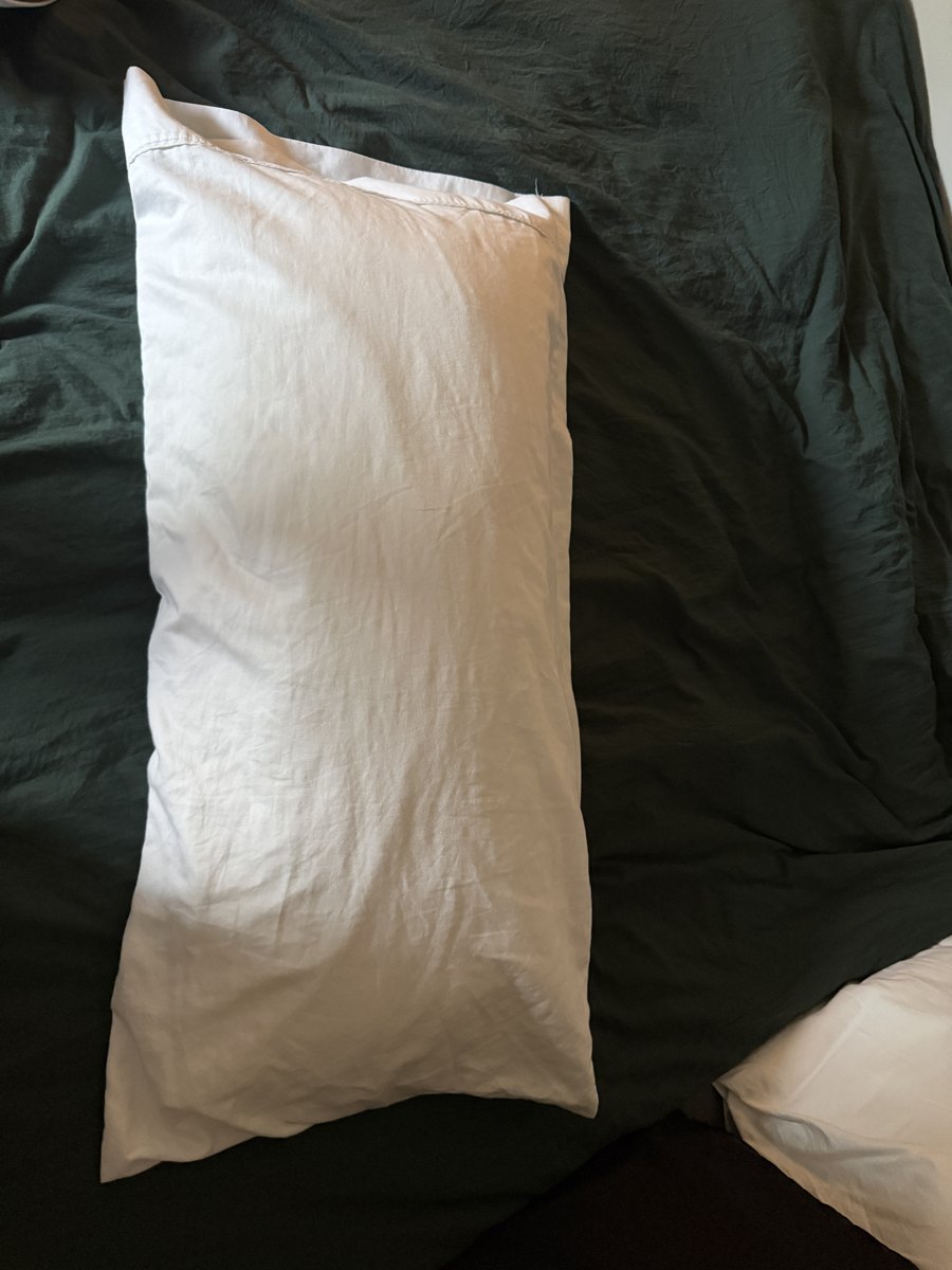 Phone photo of a plain white pillow lying on a dark green duvet.